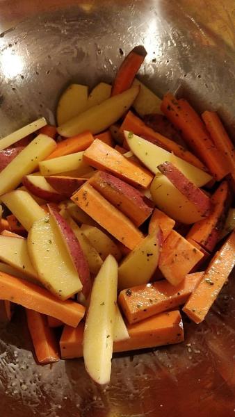 Sliced potatoes, sweet potatoes and carrots in a bowl with some oil