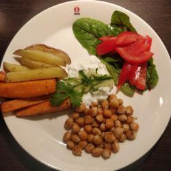 Plate with roasted vegetablels on the left, salad on the right, yogurt sauce in the center, and chickeas in the lower part of the plate